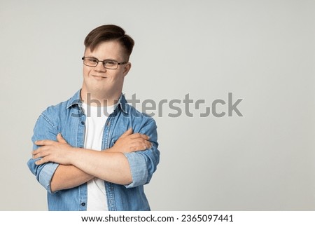 A smiling young man with cerebral palsy in glasses, jeans and a white T-shirt poses for the camera. World Genetic Diseases Day concept, place for text Royalty-Free Stock Photo #2365097441