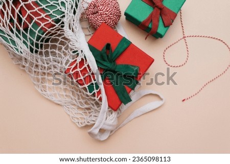 Gifts with ribbons and a skein of red and white rope lie in a white eco-friendly string bag on a beige background. Top view. Copy space.