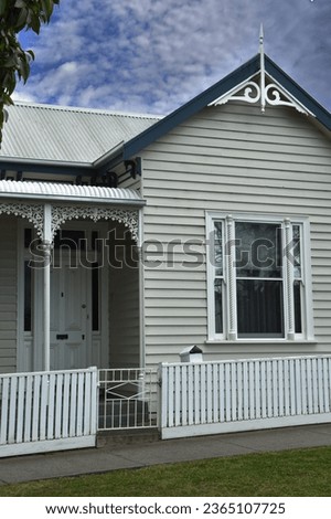 ORNATE CURLED FRETWORK GABLE ROOFED TIMBER HOME WITH A PORCH - A weatherboard wooden siding old period character style house, iron roof and cast forged metal trims on a bullnose patio verandah awning