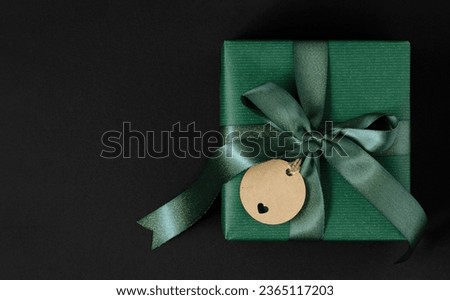 Green gift box with green ribbon and craft brown gift tag. Green background, place for your text Royalty-Free Stock Photo #2365117203