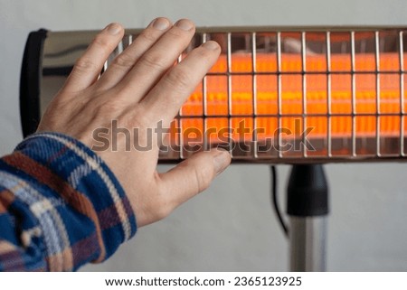  Caucasian male warming up hand near infrared heater. Space for text Royalty-Free Stock Photo #2365123925