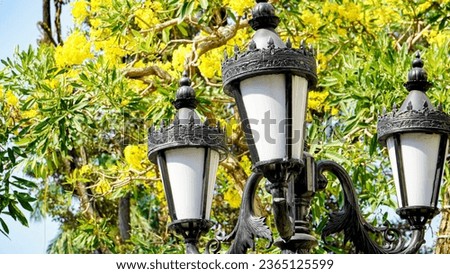 A close-up of a very classic and old garden lamp in a city park with a yellow tree in the background during the flowering season.