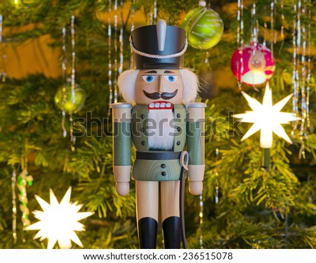 Toy soldier wooden nutcracker statue standing in front of decorated Christmas tree 