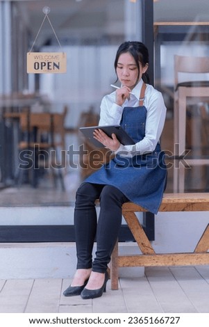 Asian business woman in an apron, the owner of the cafe stands at the door with a sign Open waiting for customers , cafes and restaurants Small business concept.