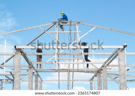Male worker on steel roof truss in construction site on blue sky background.	