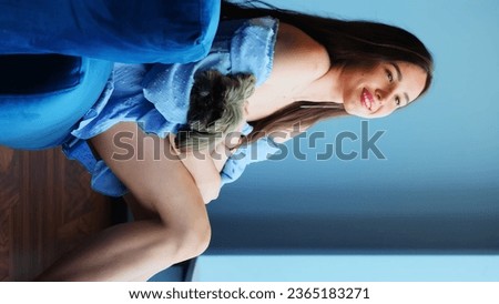 Brunette woman with shih tzu dog smiles during photosession. Woman with bare legs holds shih tzu doggy and smiles for photoshoot Royalty-Free Stock Photo #2365183271