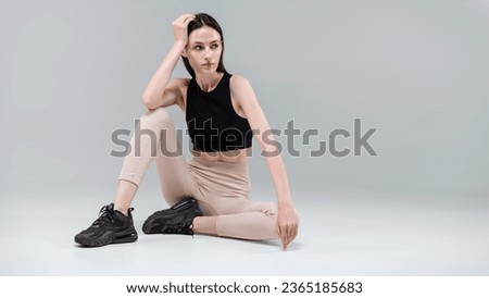 Web banner view with young model in comfy sportswear sit on floor posing for lookbook, advertising activewear, sport outfit. Woman on fitness center isolated gray copy space background looking aside Royalty-Free Stock Photo #2365185683