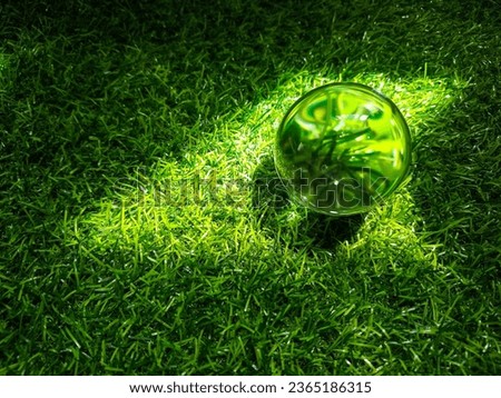 Clear glass ball on plastic grass, sunlight reflected.