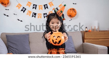 Cute little girl wearing a Halloween costume holding a pumpkin at home with happy eyes. looking at the camera.
