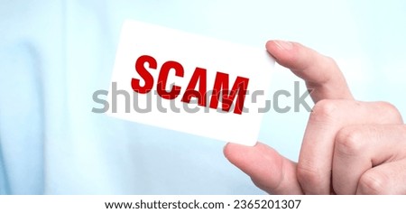 Man in blue sweatshirt holding a card with text SCAM, business concept