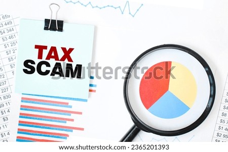 Green card on the white notepad and magnifier on the financial documentation. Text TAX SCAM. Business concept