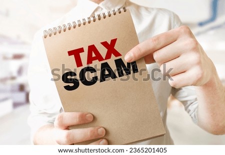 Text TAX SCAM on brown paper notepad in businessman hands in office. Business concept Royalty-Free Stock Photo #2365201405
