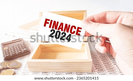 Businessman hold white card with text FINANCE 2024 Calculator, wood box, money and financial documents