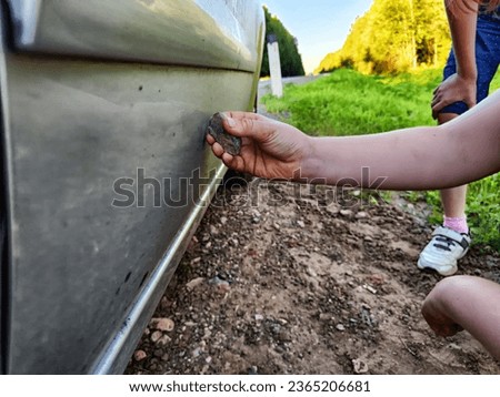 The child's hand with stone scratches the side of the car. The concept of hooliganism, property damage, disobedient boy or girl Royalty-Free Stock Photo #2365206681