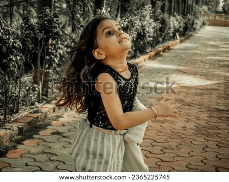 Indian little girl playing. outdoor in park. dark and light portrait filter effect image.Wearing black and white. clothes with comedy action.Blur background photo using for wallpaper.