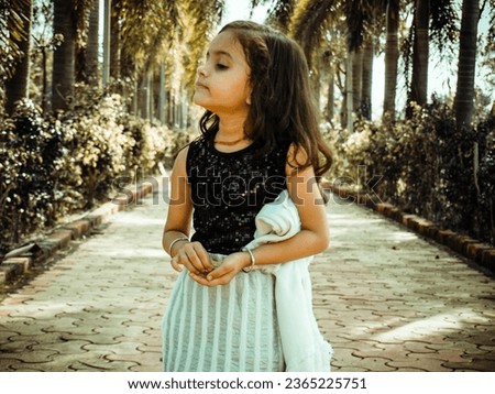 Indian little girl playing. outdoor in park.dark and light portrait filter effect image.Wearing black and white. clothes with comedy action.Blur background photo using for wallpaper.