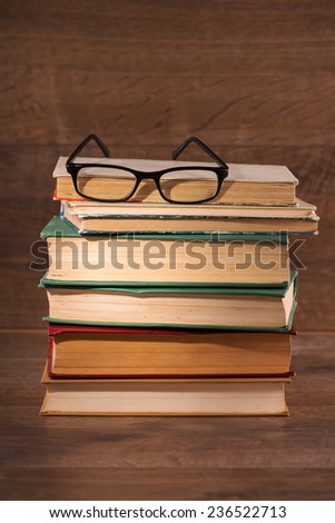 Pile of books with the glasses on the top of it lying on the wooden surface