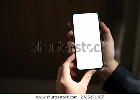 Close-up of male hand holding smartphone with white mockup on screen.