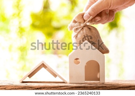 Loan for real estate concept, Man hand holding a money bag and  the  home model put on the wood in the public park.