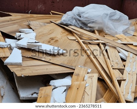 A closeup view of old flooring, drywall, and other bits of wood  chucked in a dumpster after a flood.