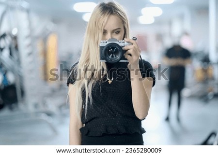 Young girl with camera in hand stands in front of the mirror, takes a selfie, A young woman takes herself to the camera through a mirror, she enjoy taking pictures of themselves.
