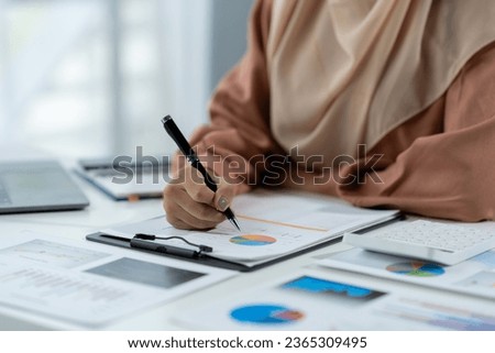Motivated muslim businesswoman wearing hijab working on real estate project analyzing documents data graphing discussing presentation business reporting in office.