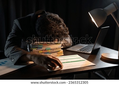 Young asian businessman sleeping on pile of paperwork laying on desk. Sleepy, tired young accountant with bills and financial papers. Graph chart laptop data in office.