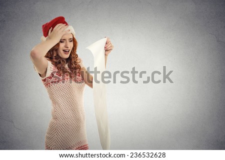 Closeup portrait Christmas woman with red Santa Claus hat screaming holding long wish list stressed out showing frustration. Negative human emotion face expression isolated grey background copy space