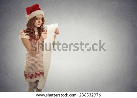 Closeup portrait Christmas woman with red Santa Claus hat holding long wish list stressed out upset showing frustration. Negative human emotion face expression isolated grey background copy space