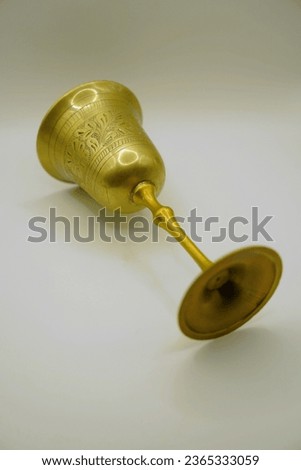 A vintage, brass chalice with a floral etching lays on its side on a white background Royalty-Free Stock Photo #2365333059