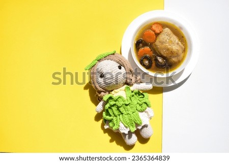 Crochet doll isolated with chicken soup in yellow and white background