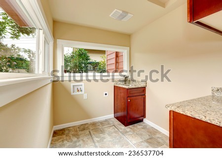 Soft tones laundry room with tile floor and cabinets. Empty space for laundry appliances