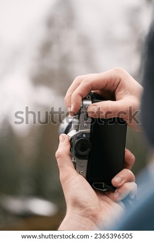 Close-up of a man holding a modern photo camera while looking at the screen. Using a Camera with the screen visible. Concept of an amateur taking photos in the mountains.