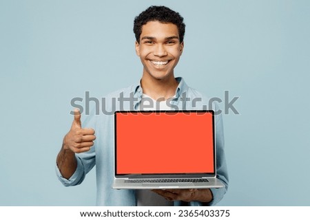 Young satisfied happy fun cheerful IT man of African American ethnicity wearing shirt casual clothes hold use work on blank screen laptop pc computer show thumb up isolated on plain blue background
