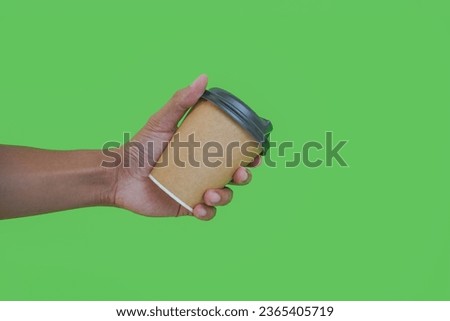 hand holding a Takeaway paper coffee cup. coffee to go in a disposable cup on a green background, you can place text or logo, kraft paper cup. 