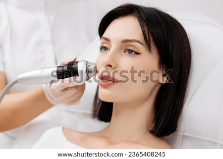 A young woman undergoes a radiofrequency facelift procedure. Advertising concept for facial skin care, anti-aging facial rejuvenation. Radio wave face lifting in a cosmetology clinic. Royalty-Free Stock Photo #2365408245