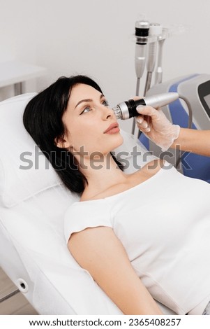 A young woman undergoes a radiofrequency facelift procedure. Advertising concept for facial skin care, anti-aging facial rejuvenation. Radio wave face lifting in a cosmetology clinic. Royalty-Free Stock Photo #2365408257