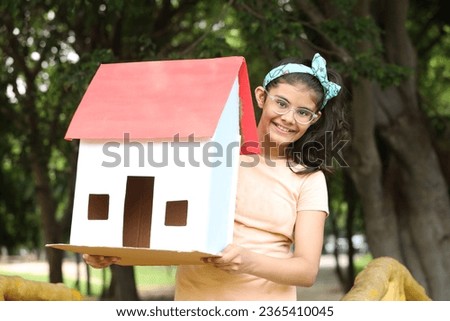 Indian happy girl holding 3D paper home shape model in park - Concept - Real Estate in India
