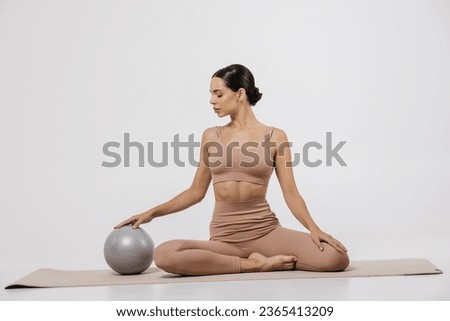 Confident fitness woman posing with medicine ball. Portrait of an attractive sportswoman holding a medical fitness ball and using it on a light studio background.