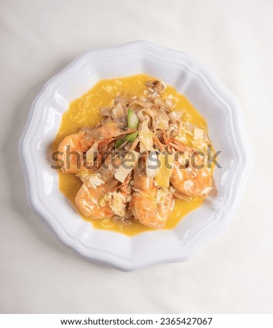 braised wok fried giant fresh tiger prawn with hot fun rice noodle and vegetables in golden yellow chicken stock cheese sauce in plate on wood table asian restaurant banquet cuisine halal food menu