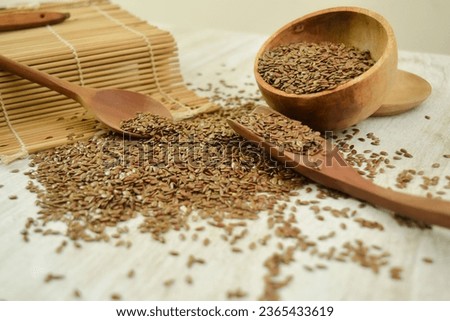 Brown Flaxseed spilled from a wooden bowl on a table with wooden spoon and sushi mat