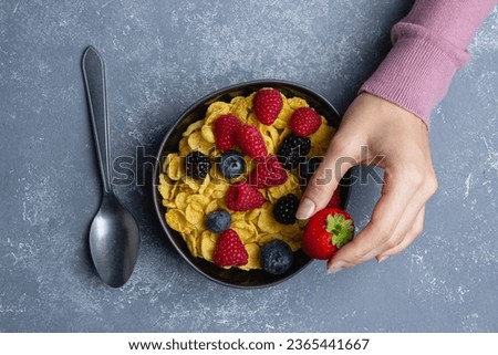 Corn flakes with berries in black bowl on blue background.