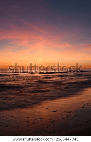 The Baltic Sea and reflections at the light of sunset. Sundown red pink sky. Long exposure photo of the sea.  Wide-angle photo. Vertical photo. 