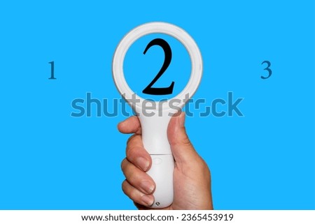 The number 2 seen enlarged through a magnifying glass. A blue background with plenty of copy space. 