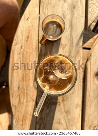 Iced latte with oat milk in a glass with straw and small cup of espresso. Directly above picture of table and iced latte on a wooden table. Refreshing drink during hot days. couple drinking coffee out