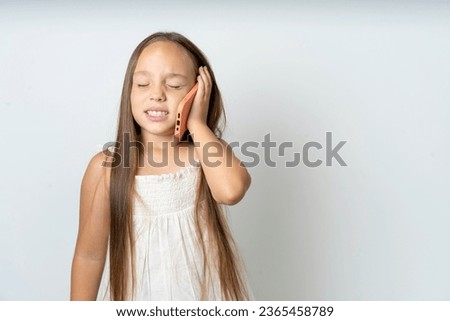 Overemotive happy Young beautiful kid girl wearing white dress laughs out positively hears funny story from friend during telephone conversation