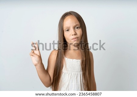 Young beautiful kid girl wearing white dress makes peace gesture keeps lips folded shows v sign. Body language concept
