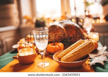 Thanksgiving day dinner with holiday autumn decor and candles. Family dining room table set with delicious golden roasted turkey on platter garnished rosemary fresh small pumpkins