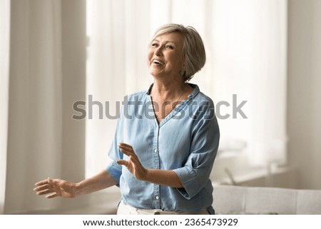Excited cheerful pretty mature woman having fun at home, enjoying activity, party, leisure, healthy joints and bones, dancing to music in modern apartment, smiling, laughing Royalty-Free Stock Photo #2365473929