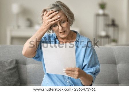 Stressed frustrated older woman getting bad news from paper letter, reading document at home, touching head in despair, panic attack, sitting on couch, receiving concerning medical result Royalty-Free Stock Photo #2365473961